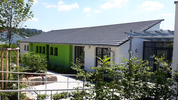 Modernes, weißes Gebäude mit leuchtend grüner Fassadenseite und dunklem Ziegeldach unter blauem Himmel.
