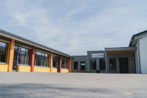 Außenansicht eines modernen Schulgebäudes mit großem Vorplatz unter bewölktem Himmel.