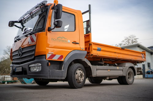 Oranger Mercedes-Benz Kipper mit "Bollmeier" Logo und Warnstreifen parkt auf Asphalt.