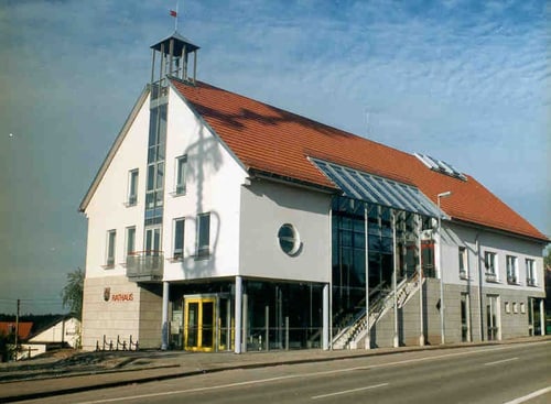 Modernes Rathaus mit rotem Ziegeldach, einem Glockenturm und Glasfassaden, Schriftzug "Rathaus".