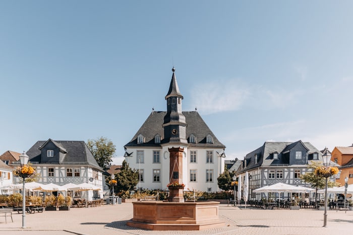 Marktplatz mit einem achteckigen Brunnen und einem turmartigen Rathaus unter blauem Himmel.