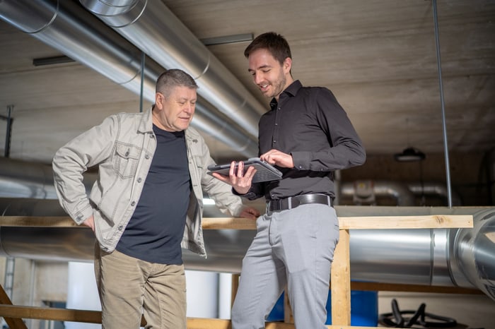 Zwei Männer in einem Heizungsraum betrachten gemeinsam ein Tablet.